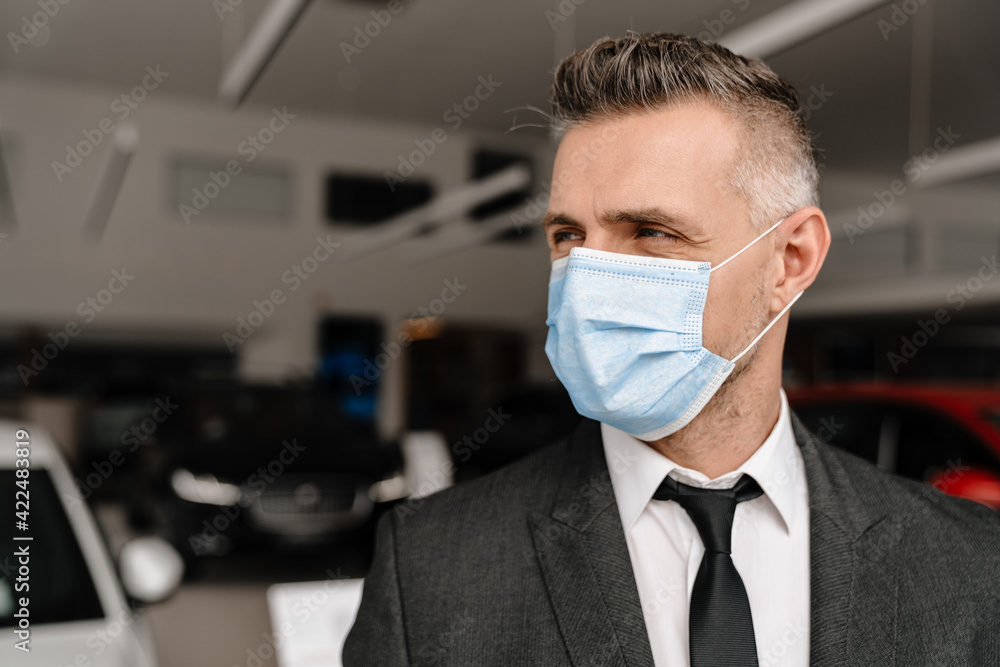 Mature man in face mask looking aside while standing at car showroom