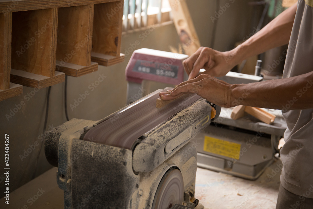 Carpenter polishes a wooden parts on a grinding machine. Close-up hands. Carpenter polishes a wooden parts on a grinding machine. Close-up hands.