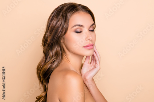 Profile side photo of young beautiful lovely peaceful woman applying cream skin care isolated on beige color background