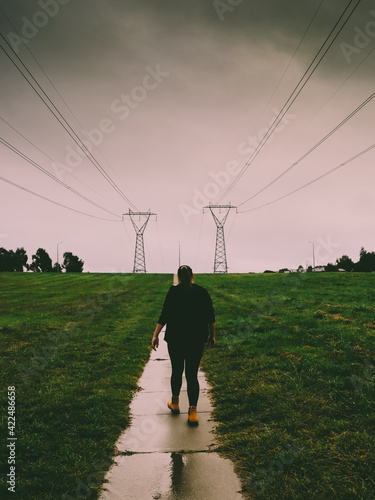 A girl with yellow boots walking on a rainy day on a path near power lines