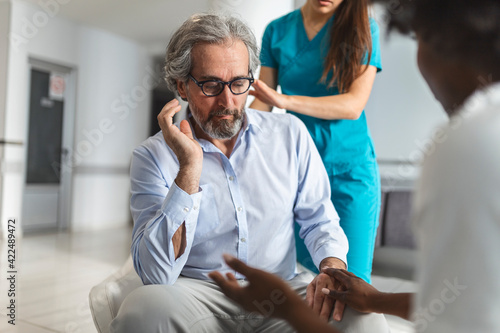 Kind female doctor embracing encouraging happy senior male patient in hospital. Happy healthy older man and his physician enjoying talking. Elderly medical health care concept.