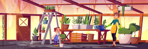 Woman and girl care plants in glass greenhouse