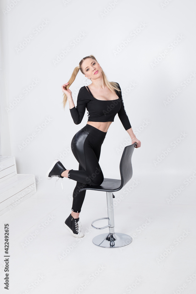 Beautiful blonde in black clothes and a black chair on a white background. Beautiful blonde in black clothes and a black chair on a white background.