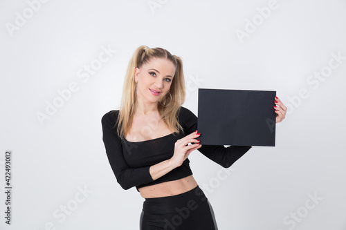 A beautiful blonde in black clothes holds a sheet of black paper in her hands. 