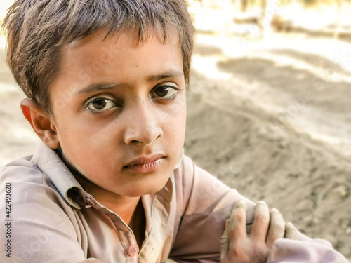 closeup of a poor staring hungry orphan boy in a refugee camp with sad expression on his face and his face and clothes are dirty and his eyes are full of pain