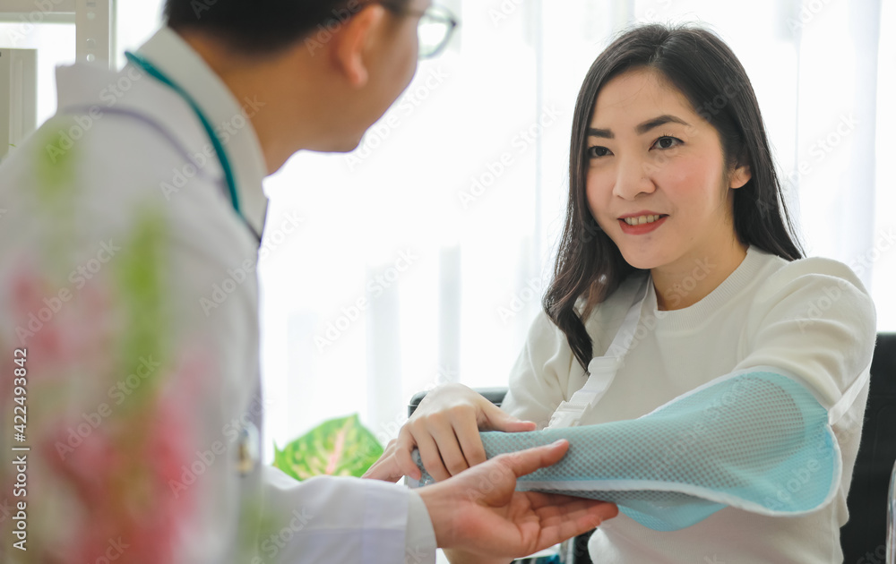 Doctor helping Asian patient with arm sling Doctor helping Asian patient with arm sling