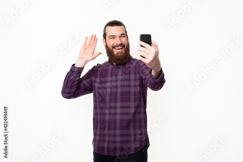 Happy smiling young bearded man talking to someone with smartphone and saluting © Vulp