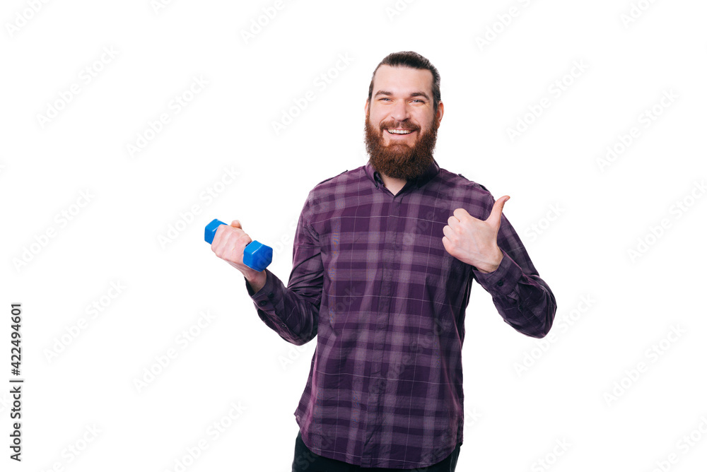 Cheerful young man in shirt showing thumb up and working with dumbbell Cheerful young man in shirt showing thumb up and working with dumbbell