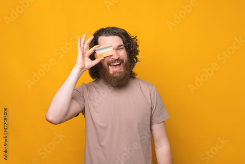 Young bearded hipster man with long curly hair showing credit card