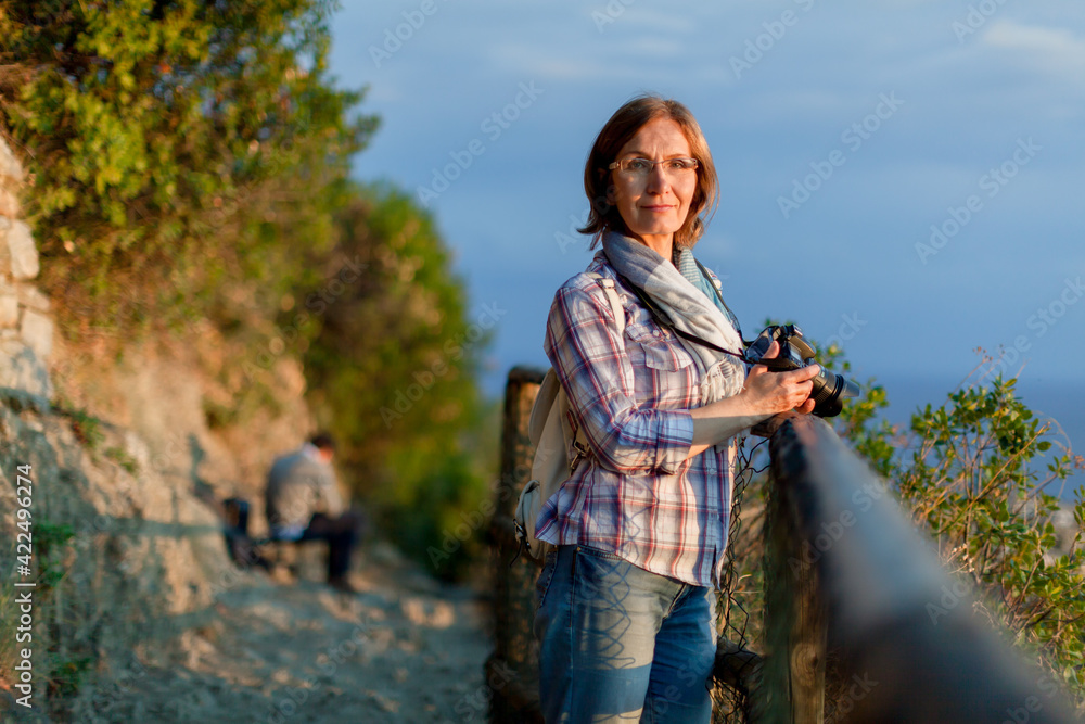 Close up portrait of lovely middle aged woman with dslr photo camera. Attractive thoughtful mature woman leaning resting on fence in the countryside. Solo domestic isolation tourism