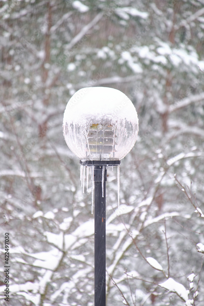 The snow-covered street lamp during the snowfall in a European city.