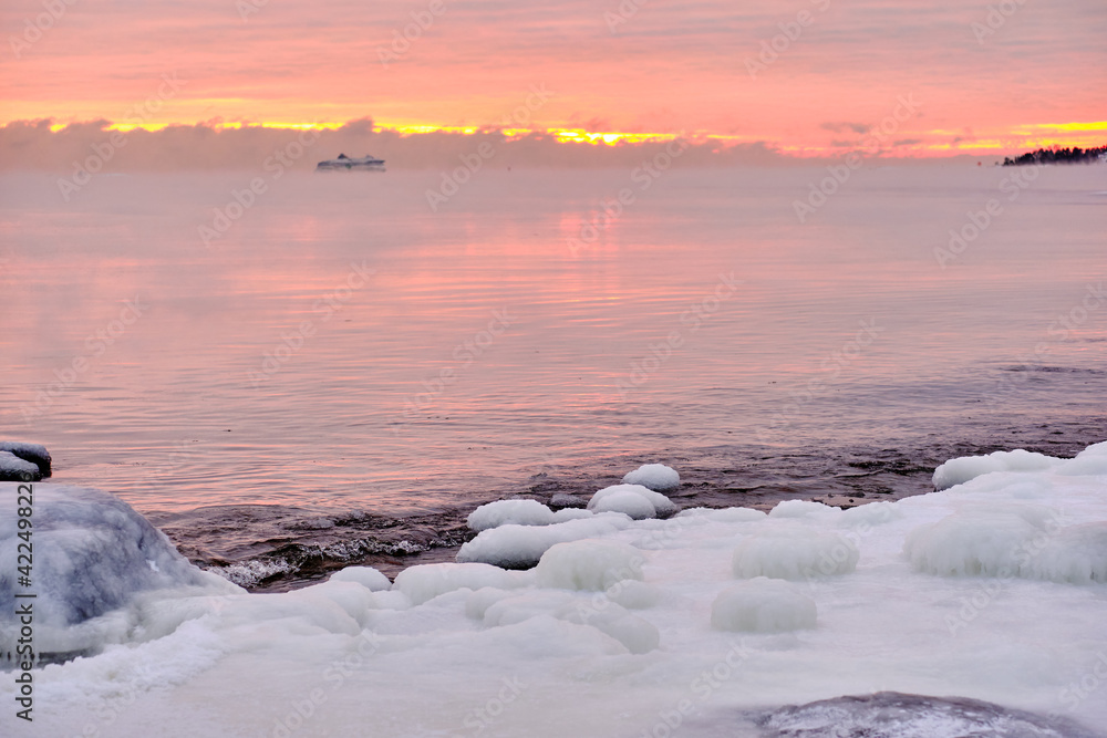 Ice-covered Baltic seashore in Finland. Fog over the sea during a strong frost in the sunset.