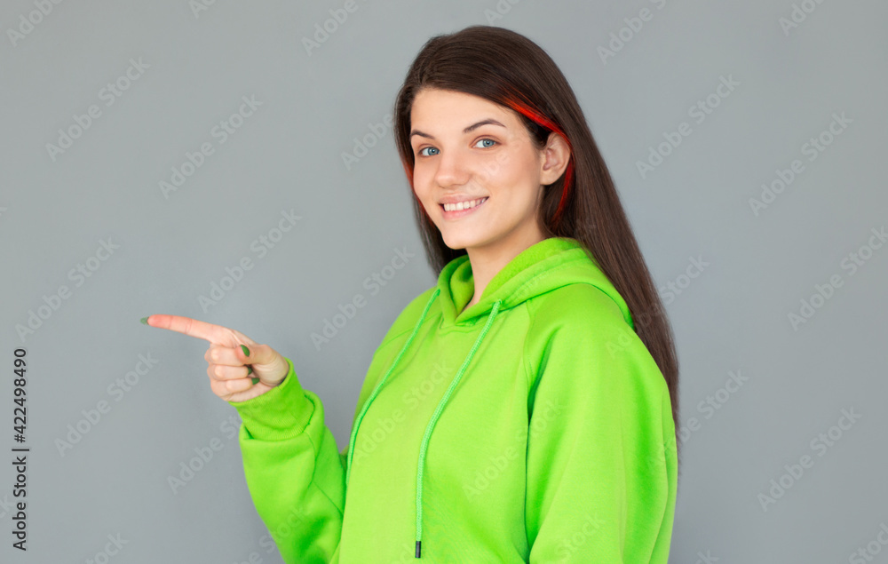 Side view of smiling woman pointing away and looking at the camera over gray background Side view of smiling woman pointing away and looking at the camera over gray background