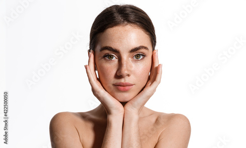 Beautiful young woman with clean perfect skin. Portrait of beauty model with natural nude make up and touching her face. Spa, skincare and wellness. Close up, white background, copyspace
