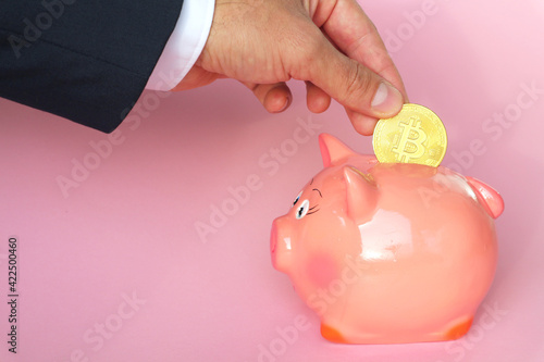 Bitcoin coin in male hand. The man lowers bitcoin into the piggy bank. Concept - investment in cryptocurrency. photo
