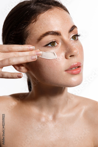 Beauty girl applying moisturizing cream on her face. Photo of young woman with flawless nude skin on white background rub scrub mask to calm down inflammation, better skin-tone