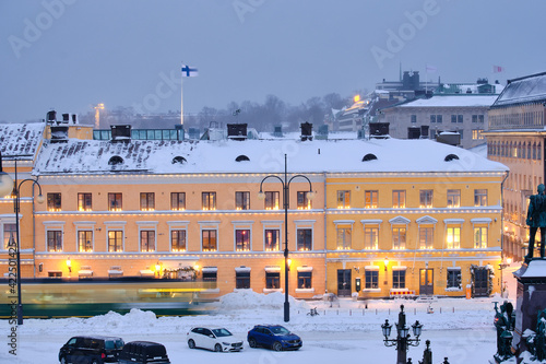 Helsinki, Finland - January 13, 2021: The tram is moving on the Senate Square during the strong snowstorm. The blue building is Helsinki City Museum