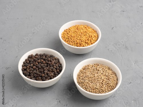 Spice black pepper, fenugreek, cumin in ceramic bowls on a white concrete background