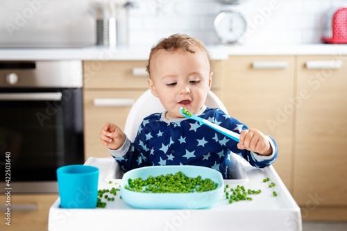 Cute baby eating grean peas with spoon photo