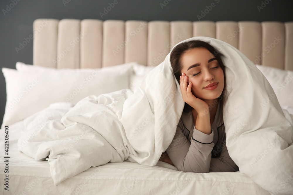 Beautiful young woman wrapped with soft blanket relaxing in bed at home Beautiful young woman wrapped with soft blanket relaxing in bed at home