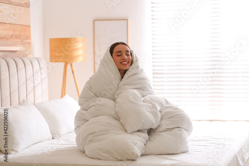 Beautiful young woman wrapped with soft blanket on bed at home