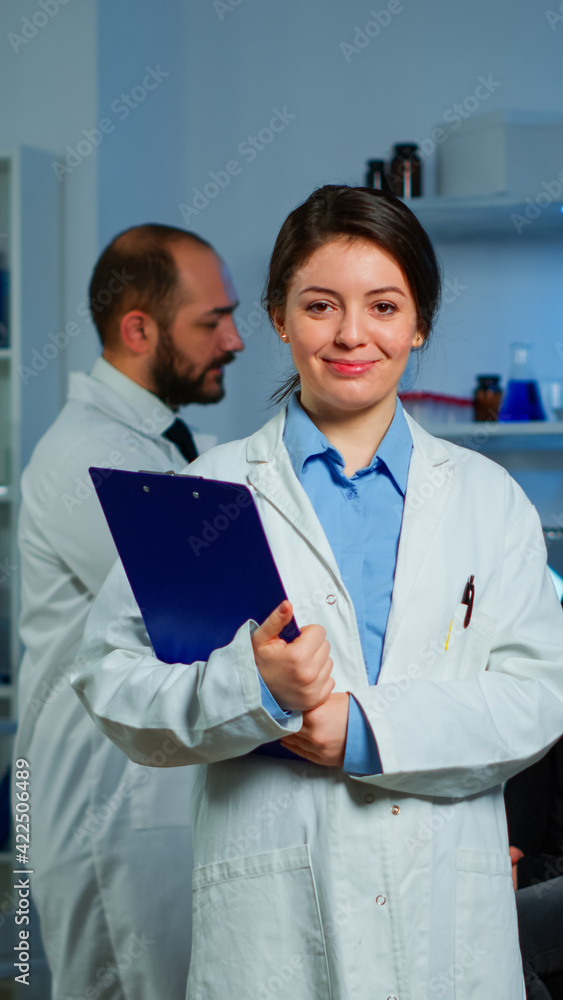 Portrait of scientist neurologist researcher looking at camera smiling while coworker discussing with patient in background about brain functions, nervous system, tomography scan working in laboratory Portrait of scientist neurologist researcher looking at camera smiling while coworker discussing with patient in background about brain functions, nervous system, tomography scan working in laboratory
