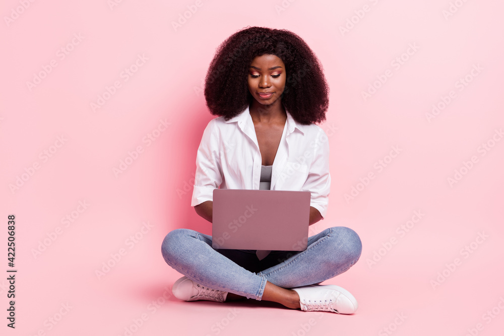 Naklejka premium Portrait of attractive focused girl sitting in lotus position using laptop typing isolated over pink pastel color background