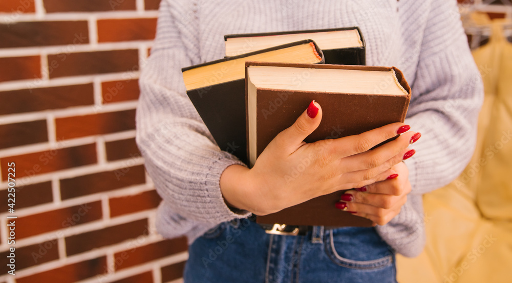 Fototapeta premium A young woman holds books in her hands. The girl is wearing a sweater and jeans.