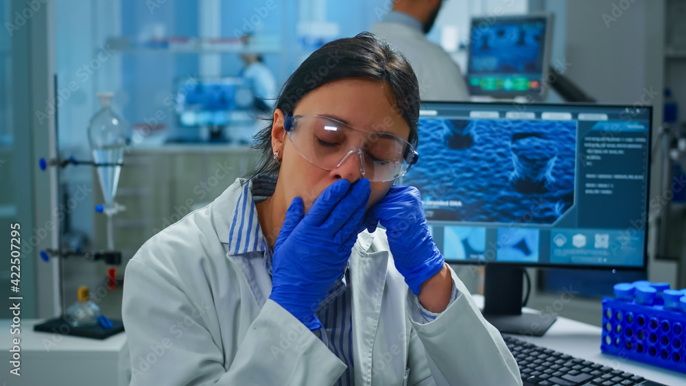 Outbreak chemist sitting in modern equipped lab looking tired at camera, yawning. Scientist examining virus evolution using high tech and chemistry tools for scientific research, vaccine development Outbreak chemist sitting in modern equipped lab looking tired at camera, yawning. Scientist examining virus evolution using high tech and chemistry tools for scientific research, vaccine development
