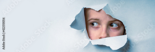 Photography Close up young cute scared child girl  looking through a hole in the paper wall
