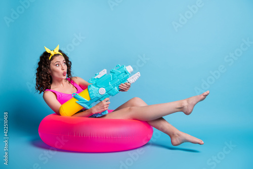 Photo of funny flirty lady wear singlet sitting circle shooting water gun lips plump looking empty space isolated blue color background