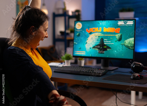 Winner player sitting on gaming chair at desk and playing space shooter video games with joystick. Woman streaming online videogames for esport tournament in room with neon lights