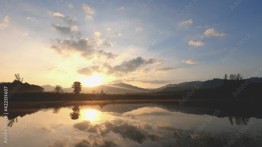 beautiful sunrise sky in spring morning at the lake. bright sunshine over blue sky and reflection of trees and orange color of morning sun in the water surface. clouds moving fast in wide space. beautiful sunrise sky in spring morning at the lake. bright sunshine over blue sky and reflection of trees and orange color of morning sun in the water surface. clouds moving fast in wide space.