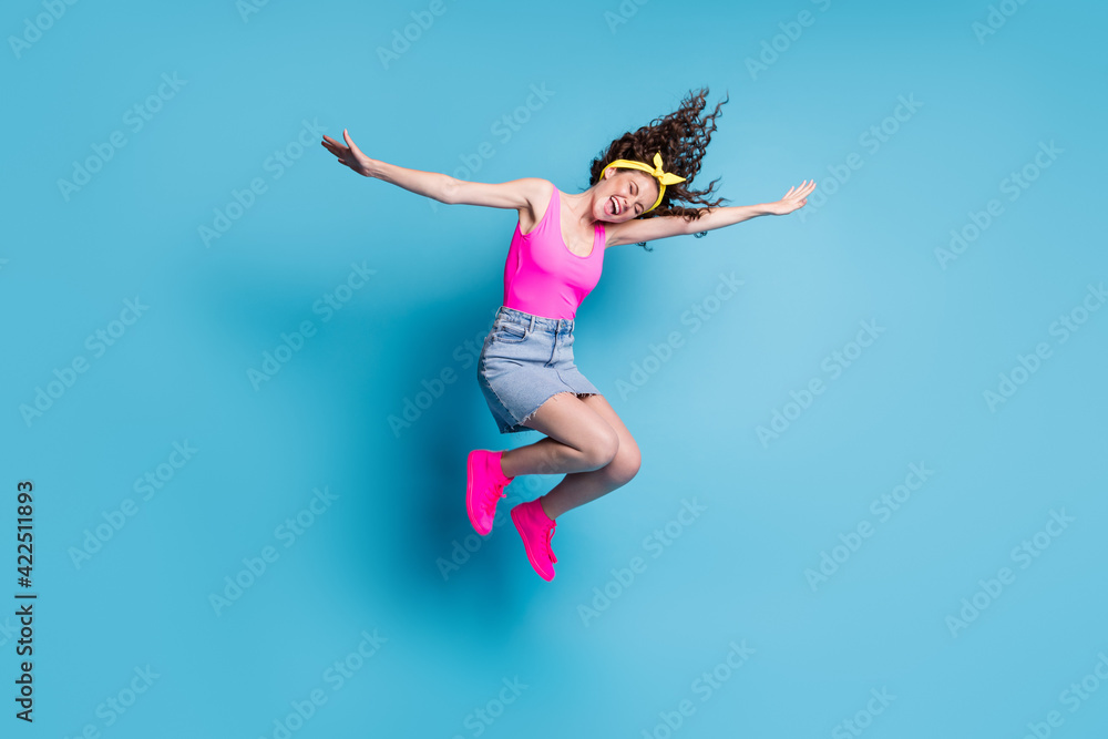 Full length photo of young excited girl happy positive smile have fun hands wind jump up fly isolated over blue color background Full length photo of young excited girl happy positive smile have fun hands wind jump up fly isolated over blue color background