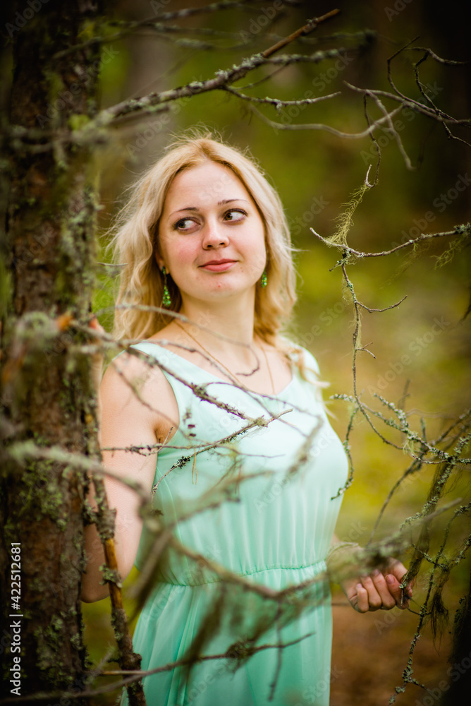 Young beautiful blonde in a light green dress posing in the woods in summer, selective focus Young beautiful blonde in a light green dress posing in the woods in summer, selective focus