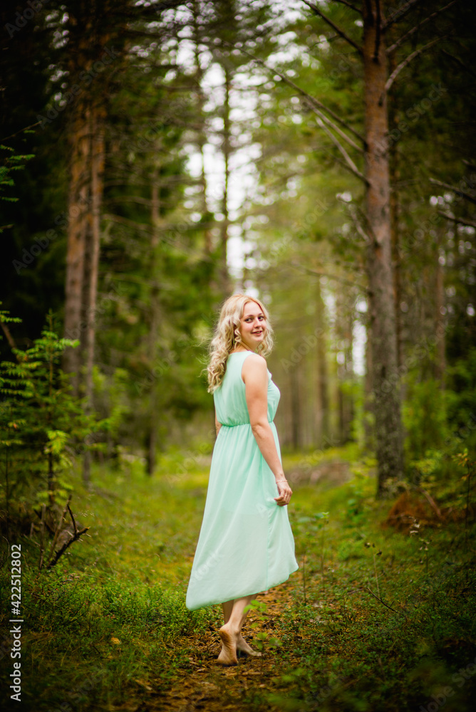 Young beautiful blonde in a light green dress posing in the woods in summer, selective focus