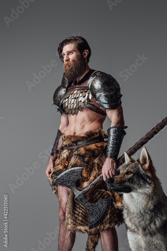 Brown haired naked viking wearing armoured clothing poses with a wolf