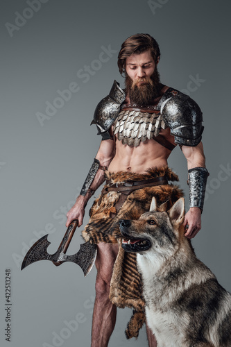 Furious northern soldier holding a double axe and posing with a wolf