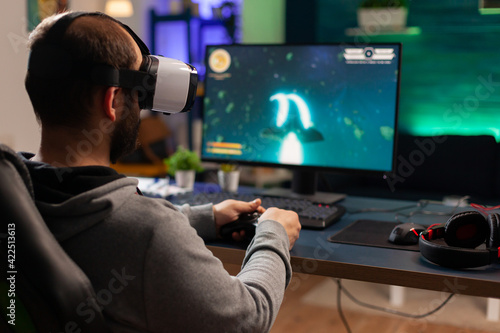 Back view of gamer playing space shooter competition using virtual reality goggles. Competitive player using joystick for online championship sitting on gamining chair late at night in living room © DC Studio