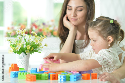  little daughter and happy mother playing with colorful plastic blocks at home