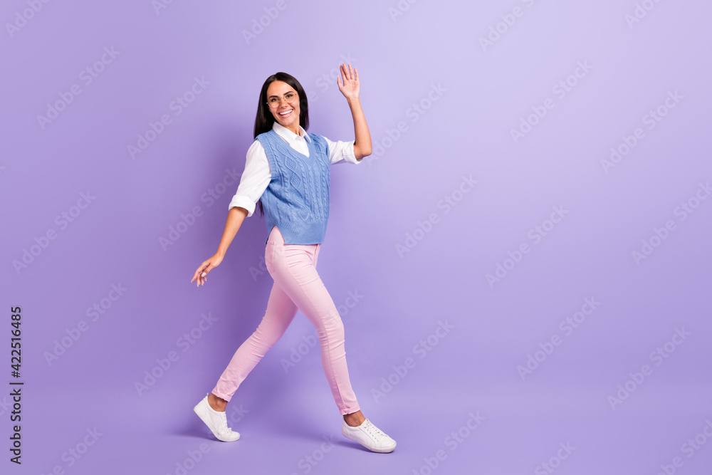 Full length body size view of attractive cheerful friendly girl walking waving you hello greetings isolated over purple violet color background Full length body size view of attractive cheerful friendly girl walking waving you hello greetings isolated over purple violet color background