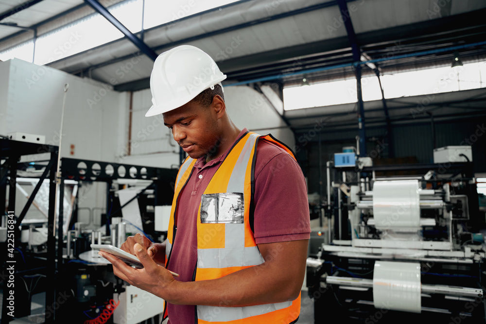 Factory employee checking portable device while examining machinery in industry Factory employee checking portable device while examining machinery in industry