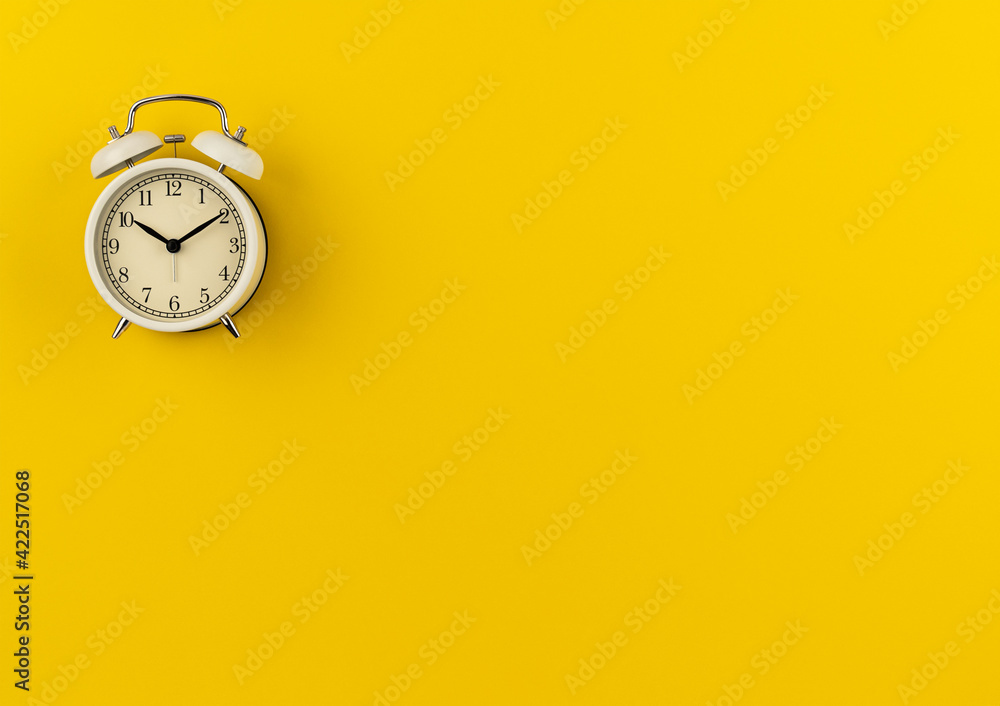 A white retro alarm clock shows ten hours and ten minutes on a yellow paper background with a copy space. Flat lay. Top view. Place for text. The concept of summer, sunny and happy time. Time: 10.10 A white retro alarm clock shows ten hours and ten minutes on a yellow paper background with a copy space. Flat lay. Top view. Place for text. The concept of summer, sunny and happy time. Time: 10.10