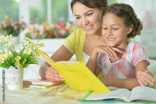 little cute girl reading book with mother at the table at home