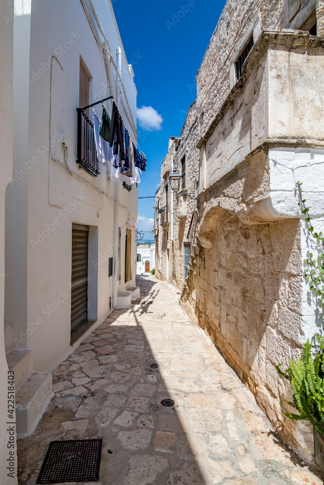 Laundry and shadows, Puglia, Italy under the clear blue sky of a sunny summer day, travel photography, street view of narrow pedestrian street covered by stone tiles. No people in the frame