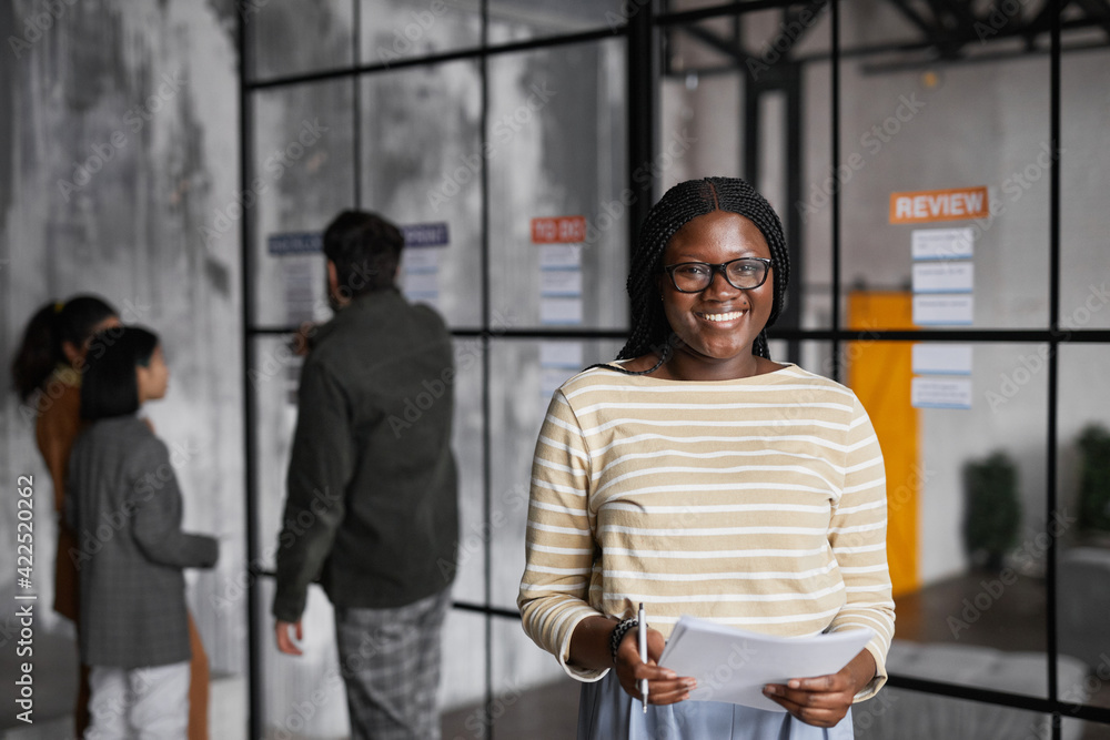 Waist up portrait of young African-American businesswoman standing by glass wall while planning project in modern office, copy space Waist up portrait of young African-American businesswoman standing by glass wall while planning project in modern office, copy space