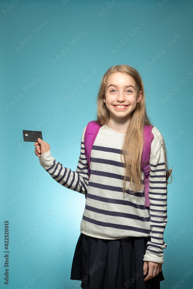Portrait of a cheerful schoolgirl caucasian with a credit card in her hands. Children financial education concept. Studio shot on a light blue background. Portrait of a cheerful schoolgirl caucasian with a credit card in her hands. Children financial education concept. Studio shot on a light blue background.