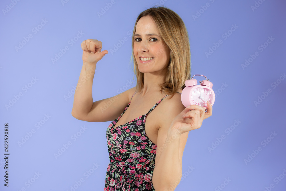 Portrait of cheerful young woman holding alarm clock and showing thumb up isolated over purple background Portrait of cheerful young woman holding alarm clock and showing thumb up isolated over purple background
