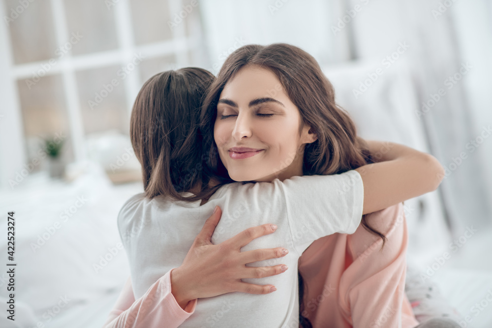 Happy mom with closed eyes hugging daughter tightly Happy mom with closed eyes hugging daughter tightly