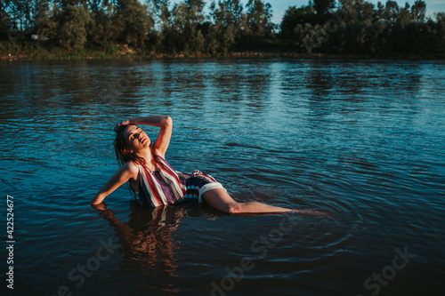 Shallow focus of a young Caucasian woman wearing a striped dress and posing in a lake in aforest photo